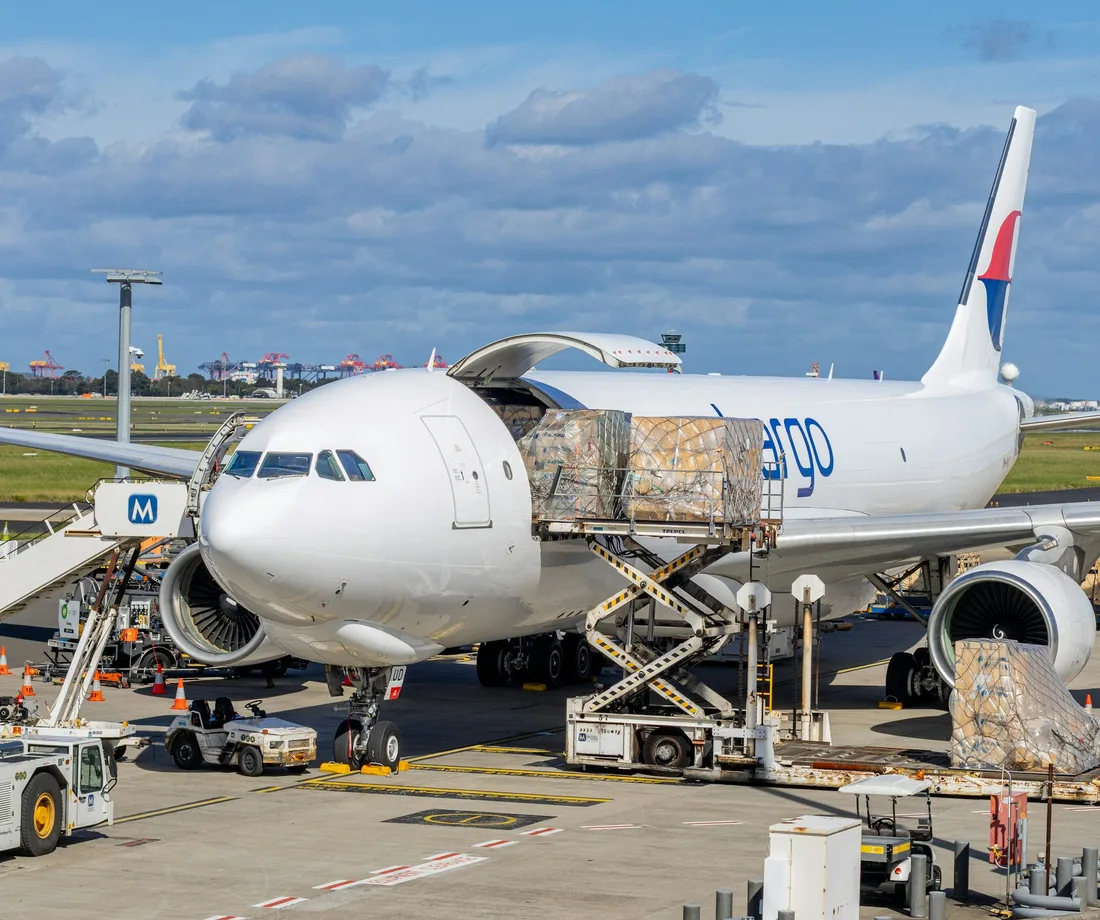 Cargo aircraft on an airport apron with loading equipment and netted freight pallets; illustrative stock photography.