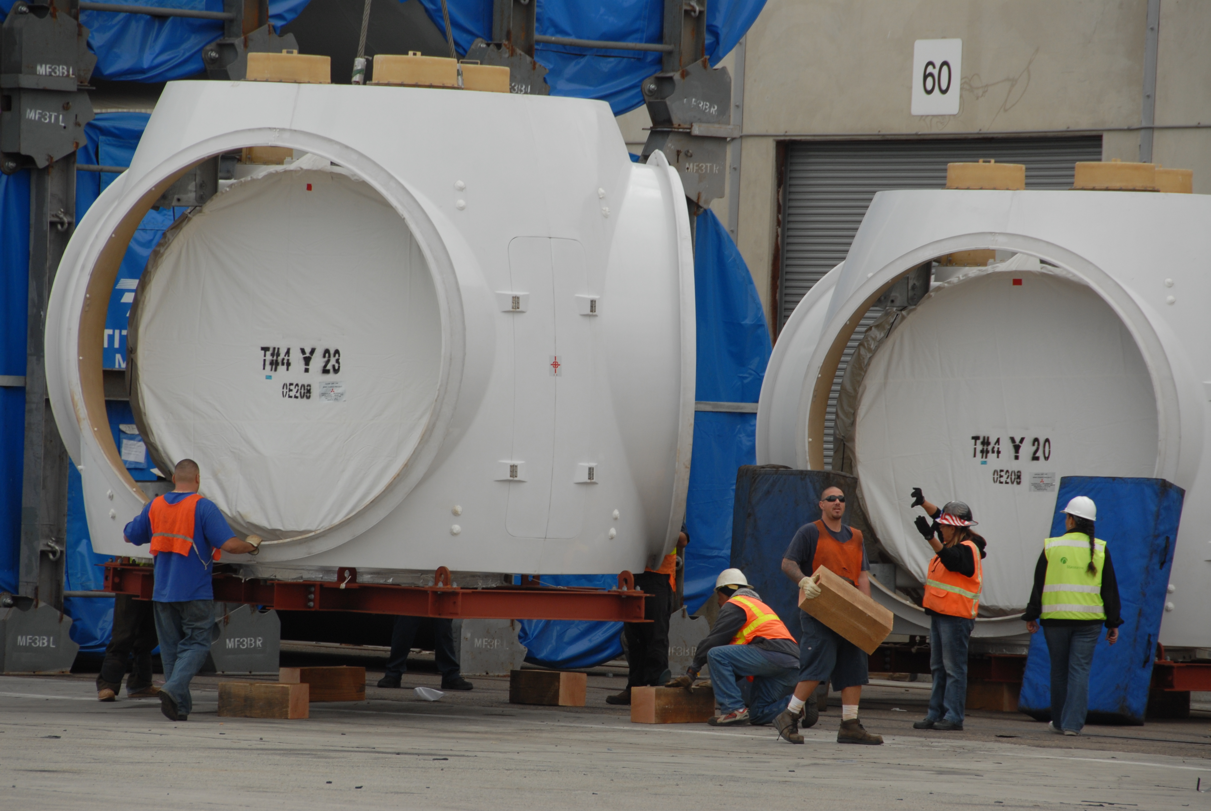 Wind turbine nacelles on transport frames with dock workers during unloading.
