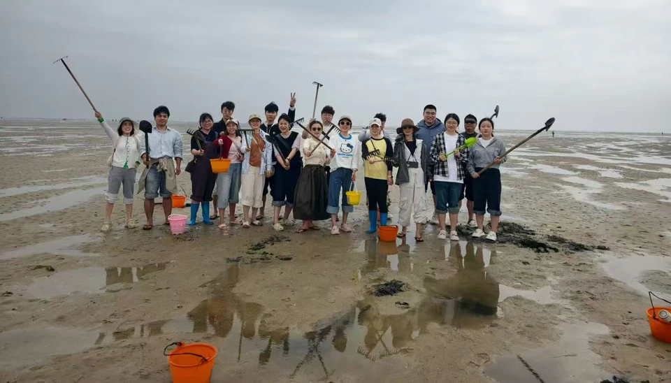 Group on a tidal flat holding rakes, shovels and buckets during an outing.